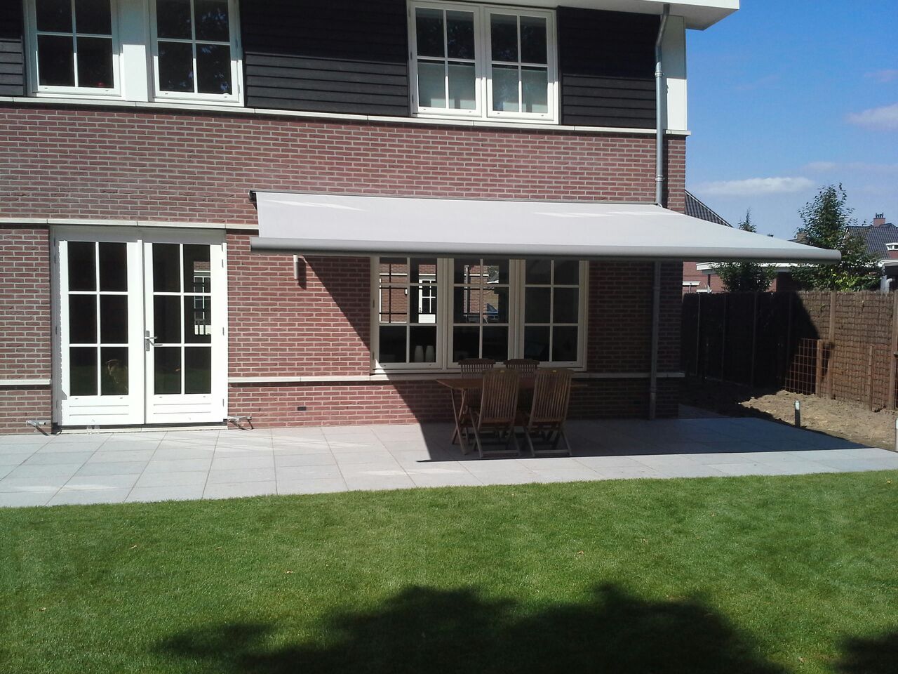 Opal zonnescherm uitgeklapt boven terras bij woning met schuine daklijn