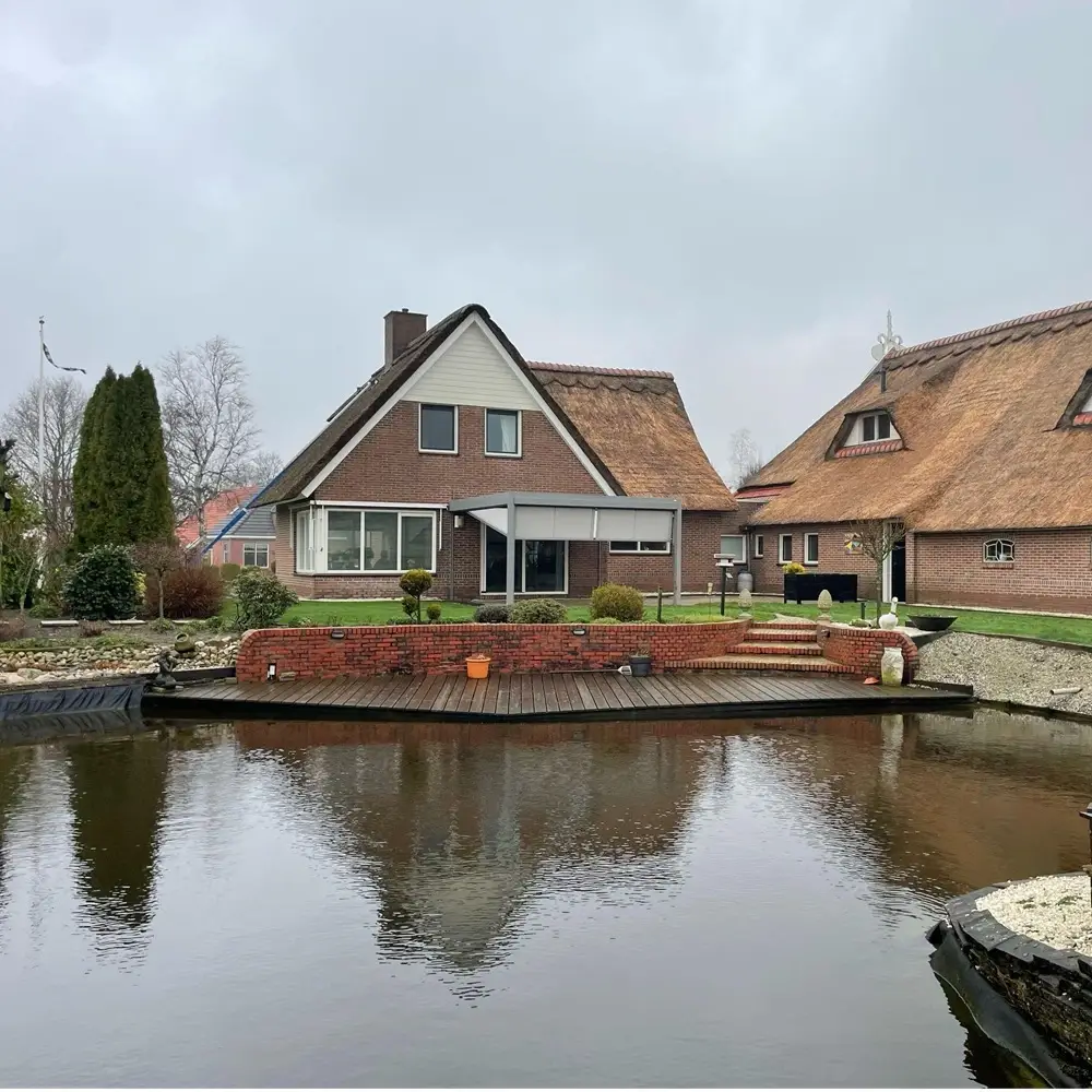 Veldman Zonwering textieloverkapping bij rietgedekte woning aan het water in Ureterp